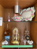 Shelf with anniversary clock in glass dome, decorative plates, porcelain bowl, and flameless votives