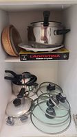 Upper shelf showing large stainless steel pot with glass lid, box labeled Lagostina, and two ceramic bowls.