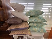 Multiple decorative cushions stacked showing leaf patterns, plain, and dotted designs.