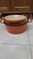 Side view of the stacked orange Le Creuset Dutch oven and pan on tiled floor.