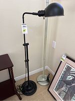 Full view of the black metal adjustable floor lamp alongside another silver floor lamp and framed art.