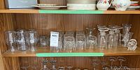 Shelf of various glass and crystalware items including stemware, rocks glasses, juice glasses, glass mugs, and crystal vases.