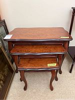 Front view of three stacked wood nesting tables showing the varying sizes and curved tabletop edges