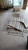Three rugs placed on carpet floor. Two smaller striped rugs partially covering larger floral patterned rug.