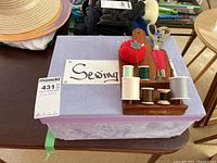 Full view of the sewing notions set with wooden holder and various thread spools, pins, and scissors on top of a purple case