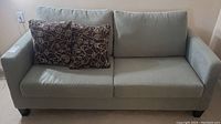 Front view of the light grey upholstered sofa bed with two brown decorative cushions on the left side.