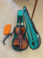 Full view of violin in open hard case, with bow and orange cloth next to it.