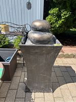 Black square pedestal with rounded stacked rock water fountain top outdoors.
