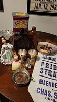 Wide view of lot items on table showing bottles, figurines, plates, and other collectibles