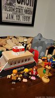 Photo of wooden Brio train transport boat with figures and gray dynamite cave piece in background; wooden train track pieces visible