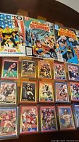 Photo showing 15 vintage 1990 football cards arranged in three rows with protective sleeves, alongside three Batman Outsiders comic books with illustrated covers.