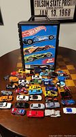 Photo showing the Hot Wheels branded traveling case with multiple toy cars arranged in front on a table.
