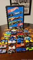 Photo showing the Hot Wheels carrying case next to a spread of about 40 die-cast cars in various colors and styles.