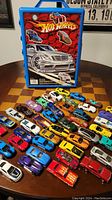 Full view of the toy cars spread out in front of the Hot Wheels carrying case with detailed flame and car illustration on the case.