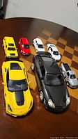 Seven model toy cars arranged on a brown wooden chessboard table, showing front and side views.
