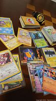 Photo showing assorted Pokemon cards scattered and stacked on a table including many recognizable Pokemon characters and an organized stack of cards.