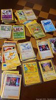 Various Pokemon trading cards grouped in multiple stacks and fanned piles on a wooden table. Cards include several Pikachu cards, standard character and trainer cards, some holographic and GX cards visible.