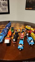Overall shot showing a collection of Thomas the Train toys and accessories on a wooden table.