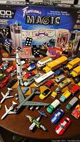 Photo showing Fantasma Magic set box with various magic props like cards, dice, and glasses in front, surrounded by many toy vehicles including buses, cars, trucks, and a model rocket.