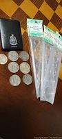 Photo showing coins, black Canada case, and three sealed plastic mint coin holders on a checkered wooden surface.