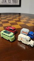 Four vintage Lesney Matchbox toy vehicles on chessboard surface, showing styles and scales