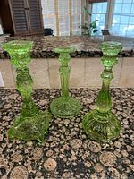 Three green glass candleholders displayed side by side on granite countertop, showing varied designs and heights