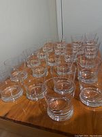 22 clear glass tumblers arranged closely on a wooden surface showing their identical shape and size.