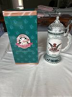 Photo of Anheuser Busch Collectors Club stein next to original green box with detailed logo and background pattern.
