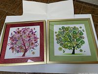 Two glass framed square prints of Trees of Life with detailed floral motifs; one with green tones and one with pink/red tones.