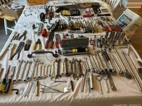 Wide view of all tools spread on table, includes wrenches, screwdrivers, pliers, socket sets, chisels, punches, and other small hand tools.
