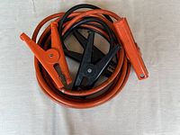 Close-up of coiled car jumper cables showing orange and black clamps and thick cable insulation.