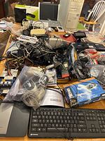Overview photo showing the mixed electronic items on a table including a beige computer tower, laptop, Gateway keyboard and touchpad, numerous tangled cables, remote controls, and other electronic accessories.