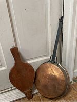Photo showing the hanging copper pan with wooden handle and the wooden and leather fireplace bellows.