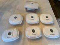 Full view of 7 FoodSaver plastic containers with vacuum seal lids arranged on table, showing variety of container sizes and shapes.