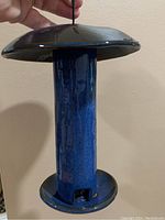 Photo showing the side view of the blue ceramic bird feeder with hanging wire, cylindrical body and wide circular top and base.