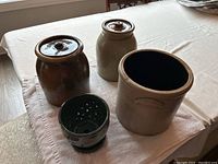 Four ceramic plant pots on a table including two large pots with lids, one large open pot, and a smaller green pot.