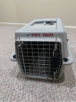 Front view showing metal wire door labeled 'Pet Taxi' with secure latching mechanism.