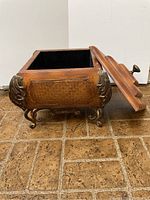 Small wooden chest with stepped lid open, showing black interior and decorative metal accents.