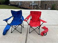 Two folding camp chairs, one red with logo and one blue, both with cup holders, with carry bags on ground