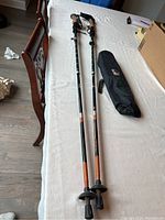 Full view of two collapsible walking sticks laid flat on a table showing ergonomic grips, orange and black coloring, tip baskets, and sections of the poles.