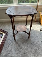 Wooden accent table standing on carpet near window, showing side view of table legs and shelf