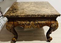 Front view of the coffee table with a square marble top showing varied brown tones and wood base with carved detail.
