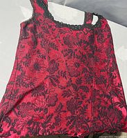 Close-up photo of a red bustier with black floral lace overlay showing the front design and strap details.