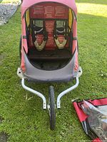 Front view into open bike trailer showing two padded shoulder harnesses, red and yellow fabric enclosure, and black mesh.