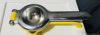 Side view of the metal and yellow plastic citrus squeezer showing the juicing bowl and handle.