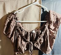 Brown crop top hanging on a white hanger, showing puff sleeves, ruffle details, and front tie.