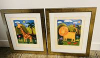 Photo showing both framed children's wall art prints, one with giraffe and one with lion, side by side against a white wall.