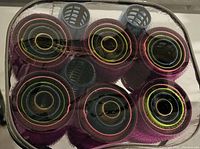 Photo showing six cylindrical mesh hair rollers with colored elastic coils, still in plastic package