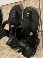Black ladies size 8 summer sandals with button details and ankle straps placed on tile floor.