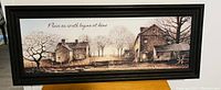 Full view of framed wall art showing rustic houses, leafless trees, fence, and inscription: Peace on earth begins at home.